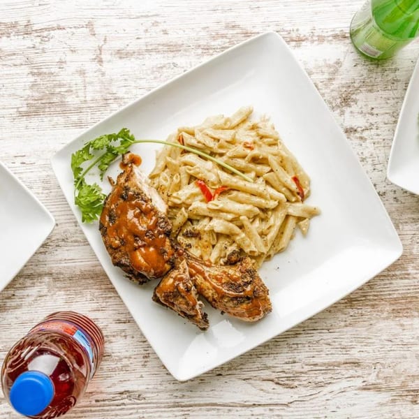 Caribbean jerk chicken with penne pasta and red peppers, garnished with cilantro on a white plate.