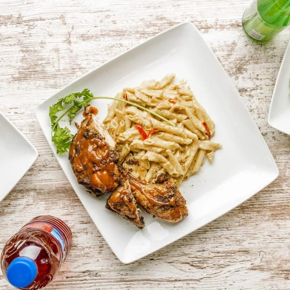Caribbean jerk chicken with penne pasta and red peppers, garnished with cilantro on a white plate.