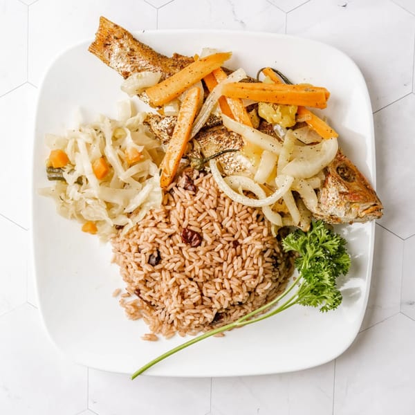 A Caribbean dish with whole fried fish, rice and peas, steamed cabbage, and sautéed vegetables.