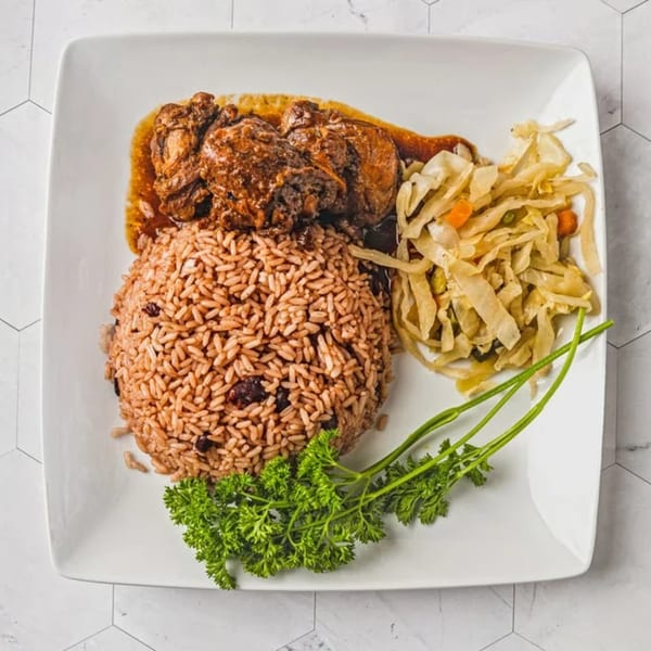 Caribbean stewed chicken, rice and peas, and steamed cabbage on a white plate.